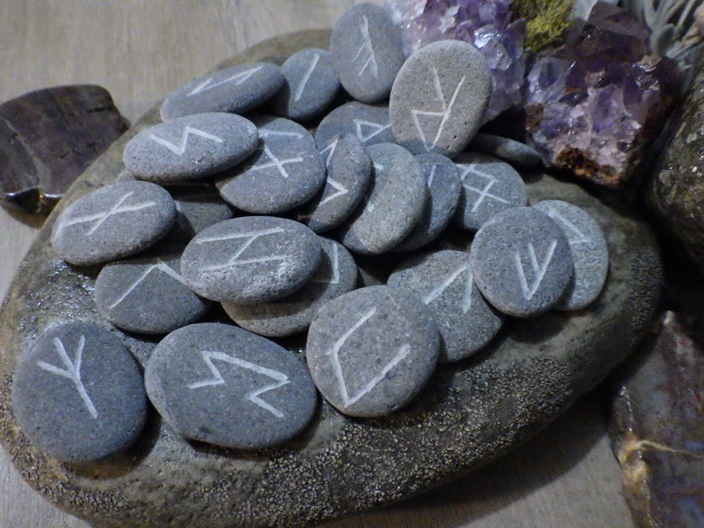 May include: A set of grey stones with white runes painted on them. The stones are arranged on a grey rock with a rough texture.
