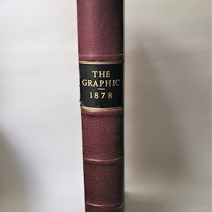 Op de afbeelding: Een bordeauxrood lederen gebonden boek met gouden letters op de rug die "THE GRAPHIC 1878" lezen.