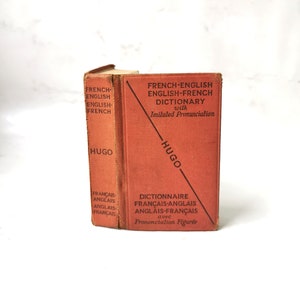 Peut inclure: Un livre relié rouge intitulé "French-English English-French Dictionary with Imitated Pronunciation" par Hugo. Le livre a une ligne diagonale noire sur la couverture et le texte "Dictionnaire Français-Anglais Anglais-Français avec Prononciation Figurée" dans le coin inférieur droit.