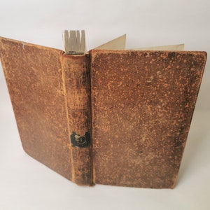 Peut inclure: Un livre relié en cuir brun avec une apparence usée et vieillie. Le dos porte un titre et le nom de l'auteur imprimés en encre noire.