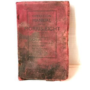 May include: A red, worn, vintage book titled "Operation Manual for the Morris Eight" with the words "Servicing, Maintenance and Adjustment Instructions" printed below the title. The book has a price of 1/6.