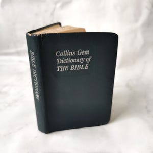 Pode incluir: Um pequeno livro encadernado em couro azul escuro intitulado "Collins Gem Dictionary of THE BIBLE".