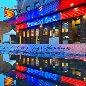 May include: A red and blue neon sign for Primanti Bros. restaurant, reflected in a puddle on the street. The sign reads "Primanti Bros."