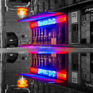 May include: A black and white photo of a storefront with a neon sign that reads "Primanti Bros." The sign is reflected in a puddle of water in front of the store.