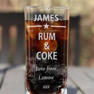 May include: A clear glass with a star design and the text "JAMES RUM & COKE" etched on the side. The glass is filled with a dark brown liquid and ice. The text "Love from Leanne xxx" is also etched on the glass.