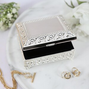 May include: A silver jewelry box with an ornate design and a black velvet interior. The box is open and the lid is propped up.