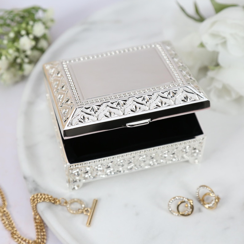May include: A silver jewelry box with an ornate design and a black velvet interior. The box is open and the lid is propped up.
