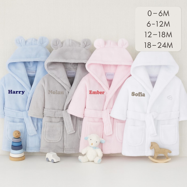 May include: Four baby bathrobes in blue, gray, pink, and white, each with a hood and a belt. The robes are personalized with names: Harry, Nolan, Ember, and Sofia. Sizes are indicated as 0-6M, 6-12M, 12-18M, and 18-24M.