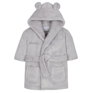 May include: A light gray plush hooded bathrobe with bear ears on the hood. The robe has a matching belt, two front pockets, and the name "Nolan" embroidered on the front. A cozy and comfortable children's garment.