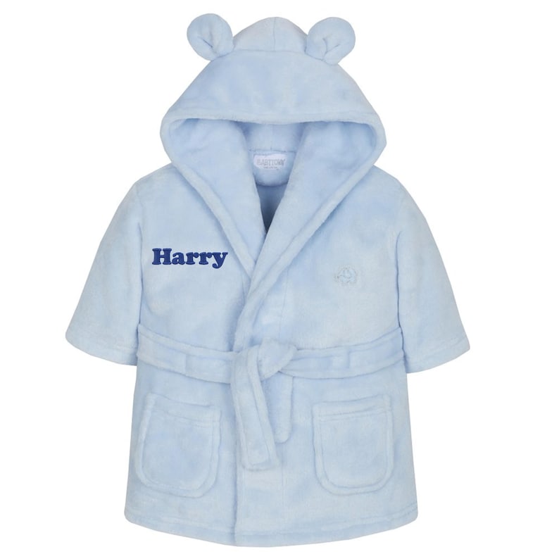May include: A light blue baby bathrobe with a hood and bear ears. The robe has a belt, pockets, and the name "Harry" embroidered on the front. The robe is made of a soft, plush material.