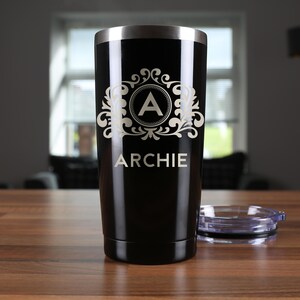 May include: A black stainless steel tumbler with a gold monogram design and the name "ARCHIE" engraved on the side.