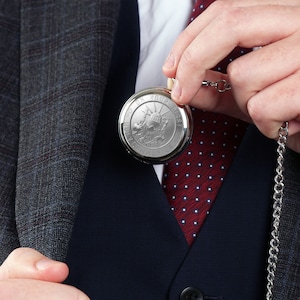 May include: A silver pocket watch with a chain. The watch face has an inscription that reads "Set On Your First Adventure".