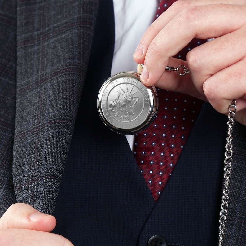 May include: A silver pocket watch with a chain. The watch face has an inscription that reads "Set On Your First Adventure".