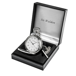 May include: A silver pocket watch with a white face and black numbers in a black velvet box. The watch has a chain and a fob. The box has the words "De Walden" printed on the inside lid.