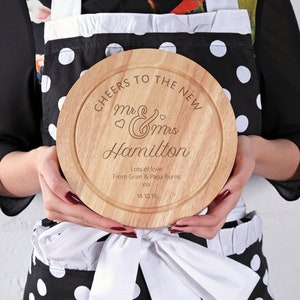 May include: A round wooden cheese board with the text "CHEERS TO THE NEW Mr & Mrs Hamilton Lots of love From Gran & Papa Burns 14.10.19" engraved on it.