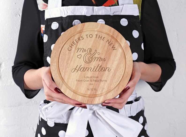 May include: A round wooden cheese board with the text "CHEERS TO THE NEW Mr & Mrs Hamilton Lots of love From Gran & Papa Burns 14.10.19" engraved on it.