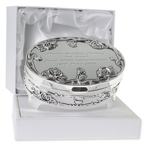 May include: Silver oval trinket box with a rose design and engraved text: "Marie Bridget Finney On Your First Holy Communion 15th May 2019". The box is sitting on a white satin-lined box.