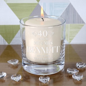 May include: A clear glass candle holder with a white candle inside. The candle has an inscription that reads "40 years as Mr & Mrs Bennett. Lots of love from the Ratcliffs xxx".