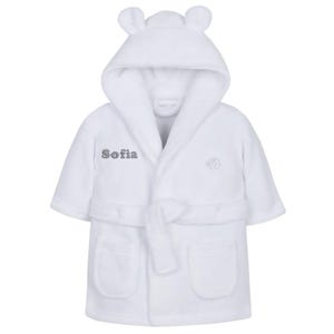 May include: A white baby bathrobe with a hood featuring small bear ears. The robe has a matching belt, two front pockets, and the name "Sofia" embroidered on the front. An elephant design is also embroidered on the front.