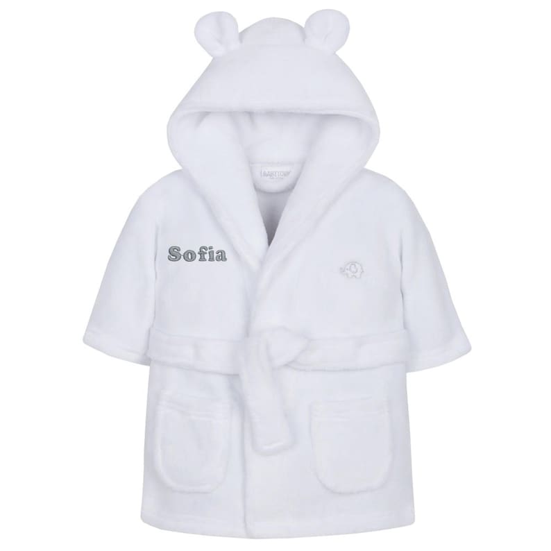May include: A white baby bathrobe with a hood featuring small bear ears. The robe has a matching belt, two front pockets, and the name "Sofia" embroidered on the front. An elephant design is also embroidered on the front.