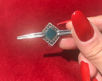 Pode incluir: Um broche de prata com uma pedra preciosa verde engastada em uma moldura quadrada cercada por pedras de marcasita.