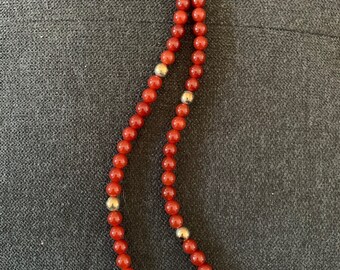 May include: A red carnelian bead necklace with gold accents. The necklace is made of round beads and has a simple design.