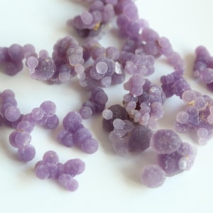 May include: A collection of purple agate stones with a grape-like cluster formation. The stones are smooth and polished, with a translucent appearance.