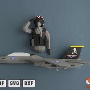 May include: A gray paper model of a fighter jet with a skull and crossbones on the tail fin. The text "TOP GUN" is printed on the tail fin. The jet has a yellow stripe on the tail fin and the number "200" on the side. A paper model of a pilot wearing a black flight suit and helmet is standing next to the jet.