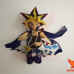 Könnte beinhalten: Eine Papierfigur eines Charakters aus der Anime-Serie Yu-Gi-Oh!. Die Figur hält eine Karte und einen Kartenhalter. Sie trägt ein schwarzes Oberteil, blaue Hosen und einen Umhang. Auf einer weißen Wand montiert.