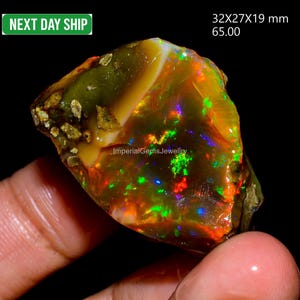 Könnte beinhalten: Ein lebendiger, roher Opal-Edelstein mit einer Mischung aus Farben wie Grün, Rot und Blau. Der Stein misst 32x27x19 mm. Das Bild enthält auch den Text "Imperial Gems Jewellery" und "Next Day Ship".
