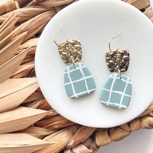 Könnte beinhalten: Ein Paar goldene und hellblaue Ohrringe mit geometrischem Muster. Die Ohrringe sind aus Polymer Clay gefertigt und haben eine gehämmerte Goldoberfläche.