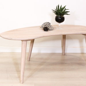 May include: A light wood coffee table with a unique, organic shape and four tapered legs. The table is made of natural wood and has a light, airy feel.