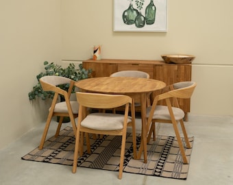 May include: A wooden dining table with four chairs, a rug, and a sideboard with a painting above it. The table is round and has a light wood finish. The chairs are also made of wood and have a light brown finish. The rug is black and white and has a geometric pattern. The sideboard is made of wood and has a dark brown finish. The painting is of a vase with flowers.