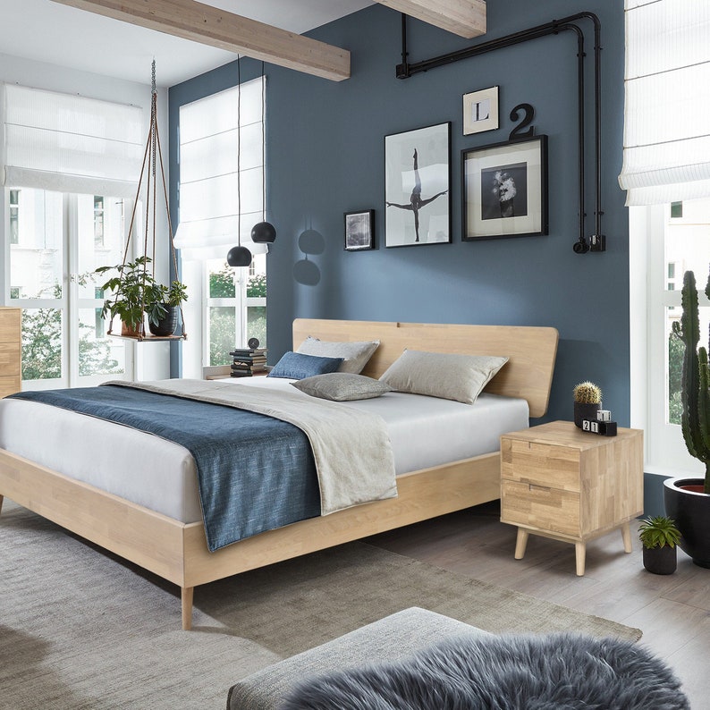 May include: A light wood bed frame with a matching nightstand. The bed has a white mattress, blue and beige bedding, and decorative pillows. The room has a blue wall, artwork, and a hanging plant.