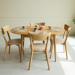 Pu&ograve; includere: Un tavolo da pranzo in legno chiaro con piano rotondo e sei sedie. Il tavolo &egrave; apparecchiato con sottopiatti, tazze e una teiera.
