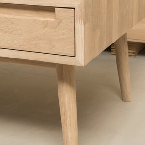 Puede incluir: Una mesa de centro de madera clara con un caj&oacute;n y cuatro patas c&oacute;nicas. El caj&oacute;n tiene un recorte rectangular para un tirador.