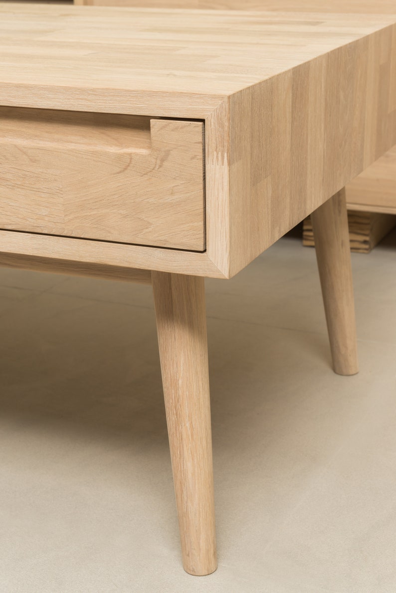 Puede incluir: Una mesa de centro de madera clara con un caj&oacute;n y cuatro patas c&oacute;nicas. El caj&oacute;n tiene un recorte rectangular para un tirador.