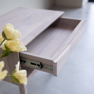May include: A white wooden nightstand with a drawer that is open, revealing a metal drawer slide. The nightstand has a simple design and is made of light wood.