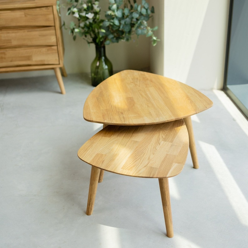 Puede incluir: Un conjunto de dos mesas nido de madera con tapa triangular. Las mesas son de madera clara y tienen un acabado natural.