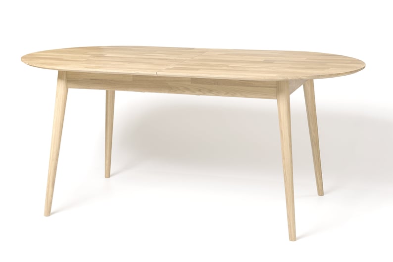 Pu&ograve; includere: Un tavolo da pranzo ovale in legno chiaro con un'estensione a foglia. Il tavolo ha quattro gambe affusolate.
