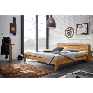 Puede incluir: Un marco de cama de madera con un acabado de madera clara. El marco de la cama tiene un cabecero con un diseño de listones. La cama está hecha con ropa de cama blanca y almohadas. La cama está en un dormitorio con una pared de ladrillo blanco y una ventana grande.