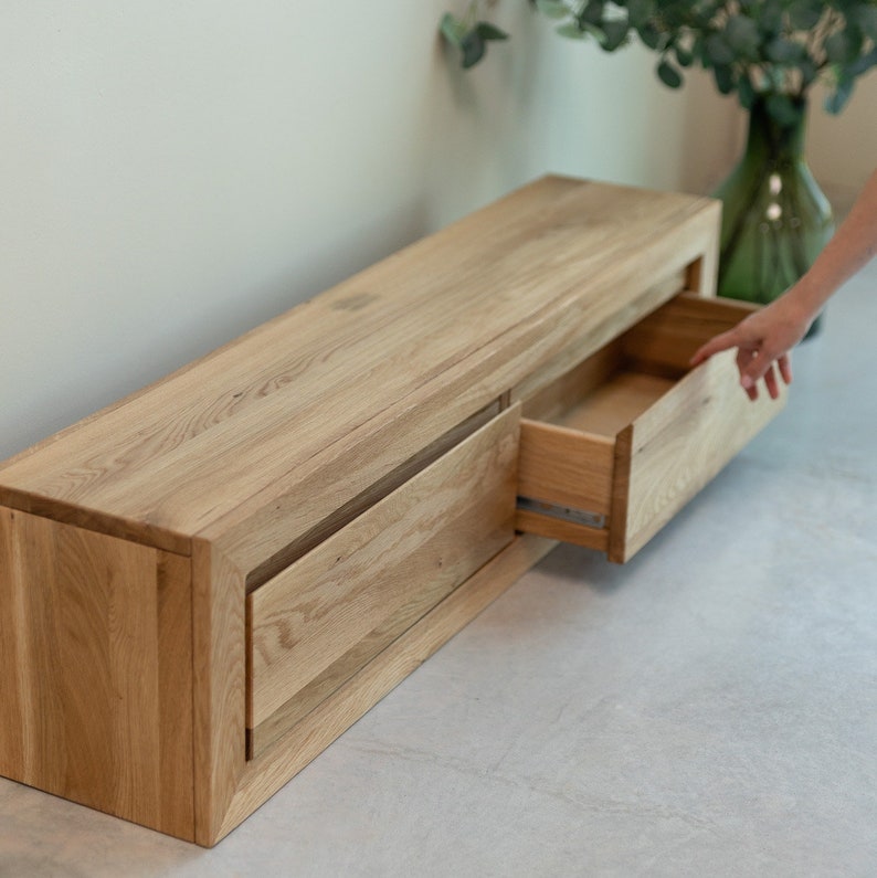 K&ouml;nnte beinhalten: Ein helles Holz-Entertainment-Center mit drei Schubladen, von denen eine ge&ouml;ffnet ist. Die Schubladen sind aus dem gleichen Holz wie das Entertainment-Center.