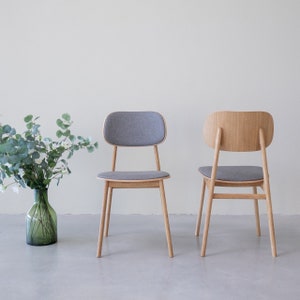 Könnte beinhalten: Zwei Holzstühle mit grauen Stoffbezügen. Die Stühle haben ein schlichtes, modernes Design und sind aus hellem Holz gefertigt.