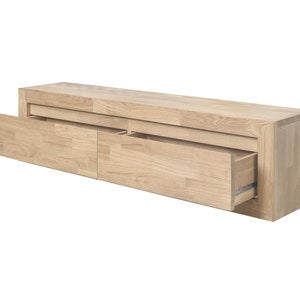 K&ouml;nnte beinhalten: Ein heller Holz-TV-Schrank mit zwei Schubladen, von denen eine ge&ouml;ffnet ist. Der Schrank hat ein schlichtes, modernes Design.