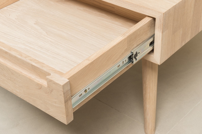 Puede incluir: Un caj&oacute;n de madera clara con un riel de caj&oacute;n de metal est&aacute; parcialmente abierto. El caj&oacute;n est&aacute; unido a una mesa de madera clara con una sola pata visible.