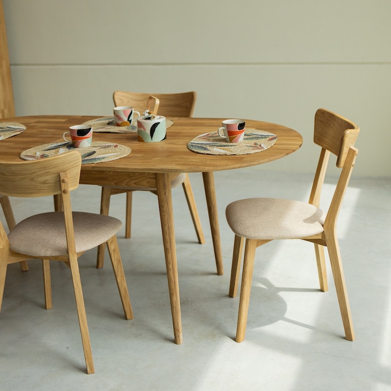 Pu&ograve; includere: Un tavolo da pranzo rotondo in legno con quattro sedie. Il tavolo ha una finitura in legno chiaro e le sedie hanno una finitura in legno naturale. Il tavolo &egrave; apparecchiato con tovagliette e tazze.