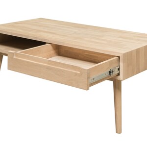 Puede incluir: Una mesa de centro de madera clara con un caj&oacute;n que est&aacute; abierto y un estante debajo. La mesa tiene cuatro patas que son c&oacute;nicas y ligeramente inclinadas.