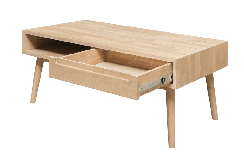 Puede incluir: Una mesa de centro de madera clara con un caj&oacute;n que est&aacute; abierto y un estante debajo. La mesa tiene cuatro patas que son c&oacute;nicas y ligeramente inclinadas.