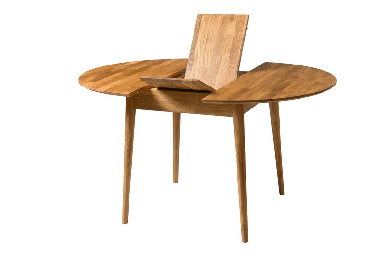 May include: A round wooden table with a leaf extension. The table has a light brown finish and four legs. The leaf is open and propped up against the table.