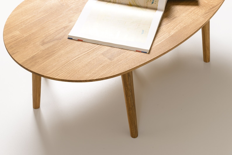 May include: A light wood oval coffee table with four slender legs. The table has a natural wood finish and is topped with a magazine.